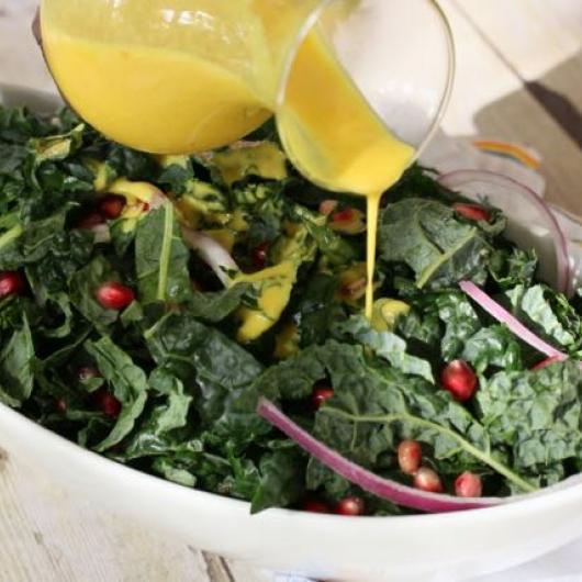 Bowl of kale salad with turmeric dressing being drizzled over